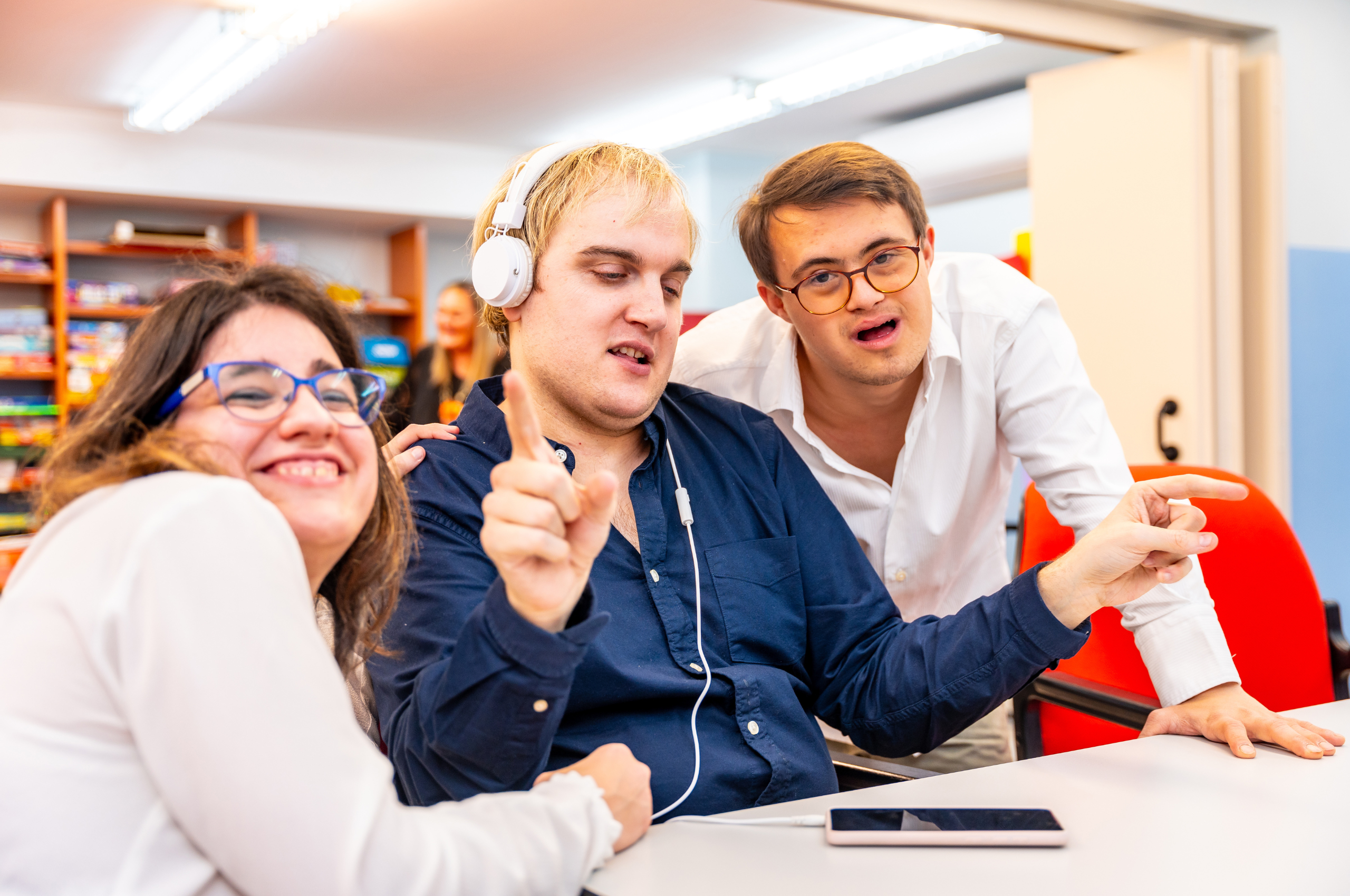 Three people with learning disabilities having fun. One person listens to headphones and is dancing, The other two people are smiling at the camera.